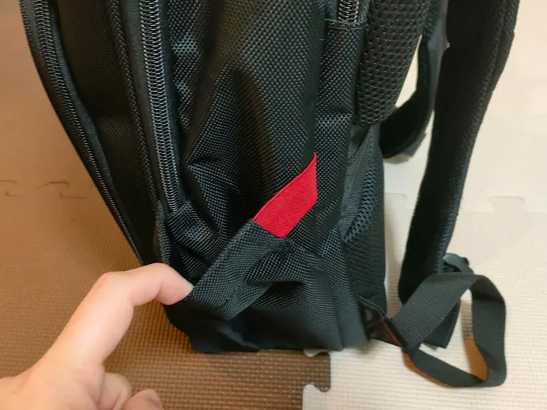 黒いリュックサックの側面のポケットを指で開けている様子 赤いタグが見える