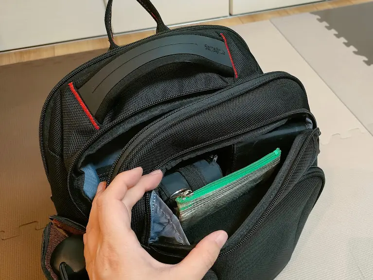 Samsonite黒いバッグの開いたポケットに入っている緑のポーチと手