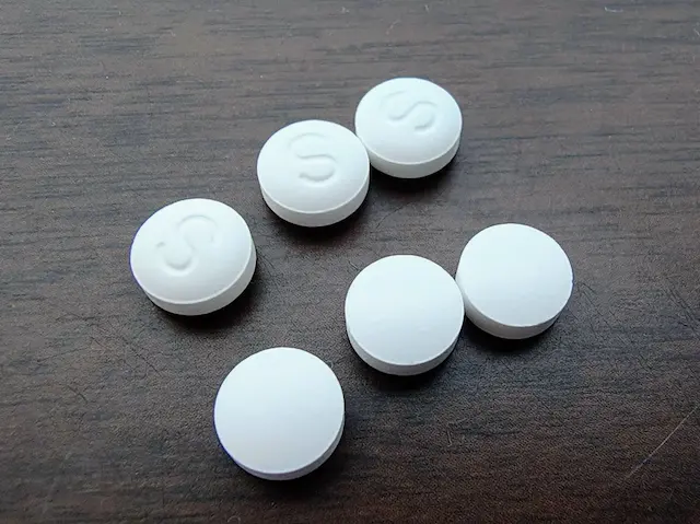 茶色い木目調の台の上に置かれた6つの白い錠剤 3つにはSの文字が刻印されており 3つは無地